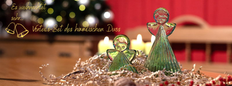 je 1 kleiner und großer Engel aus grünem Thüringer Waldglas auf hellem Holztisch mit weihnachtlicher Deko und im Hintergrund funkelndem Weihnachtsbaum