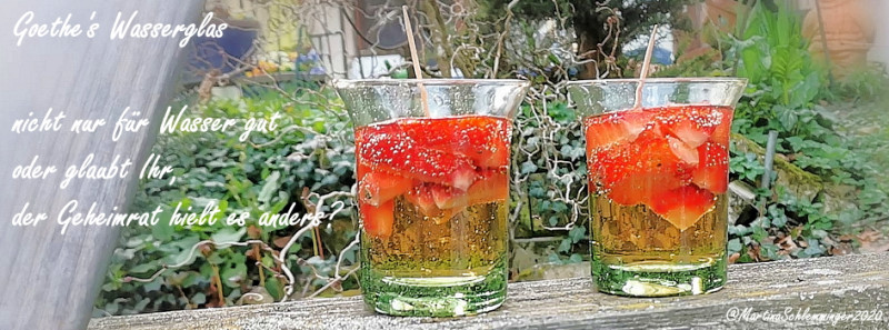 2 grüne Thüringer Waldglas Goethewassergläser gefüllt mit Erdbeerbowle vor Grün im Garten auf einem verwitterten Holzbalken